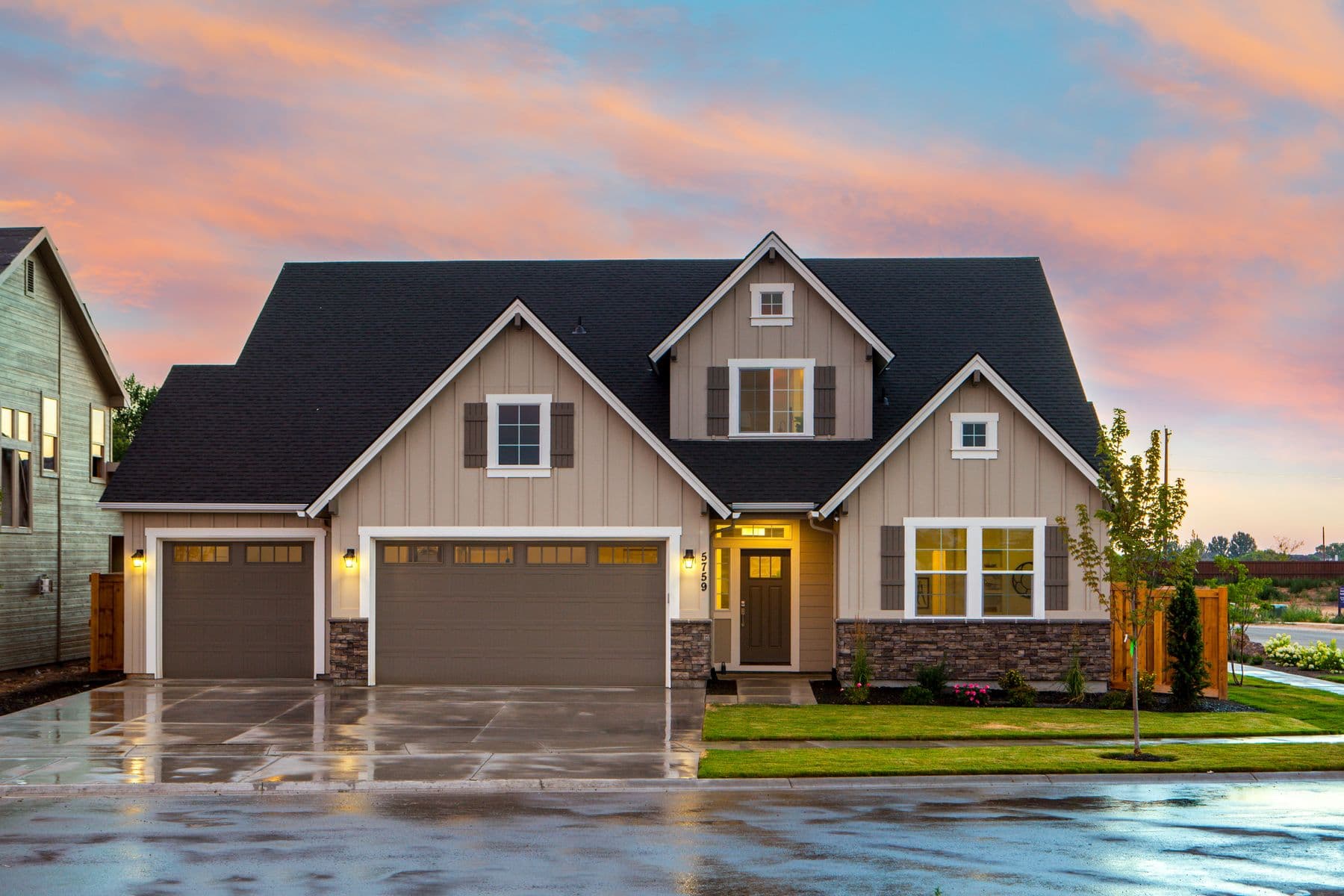 Craftsman home at dusk with stone veneer, a landscaped lawn, and a concrete driveway.