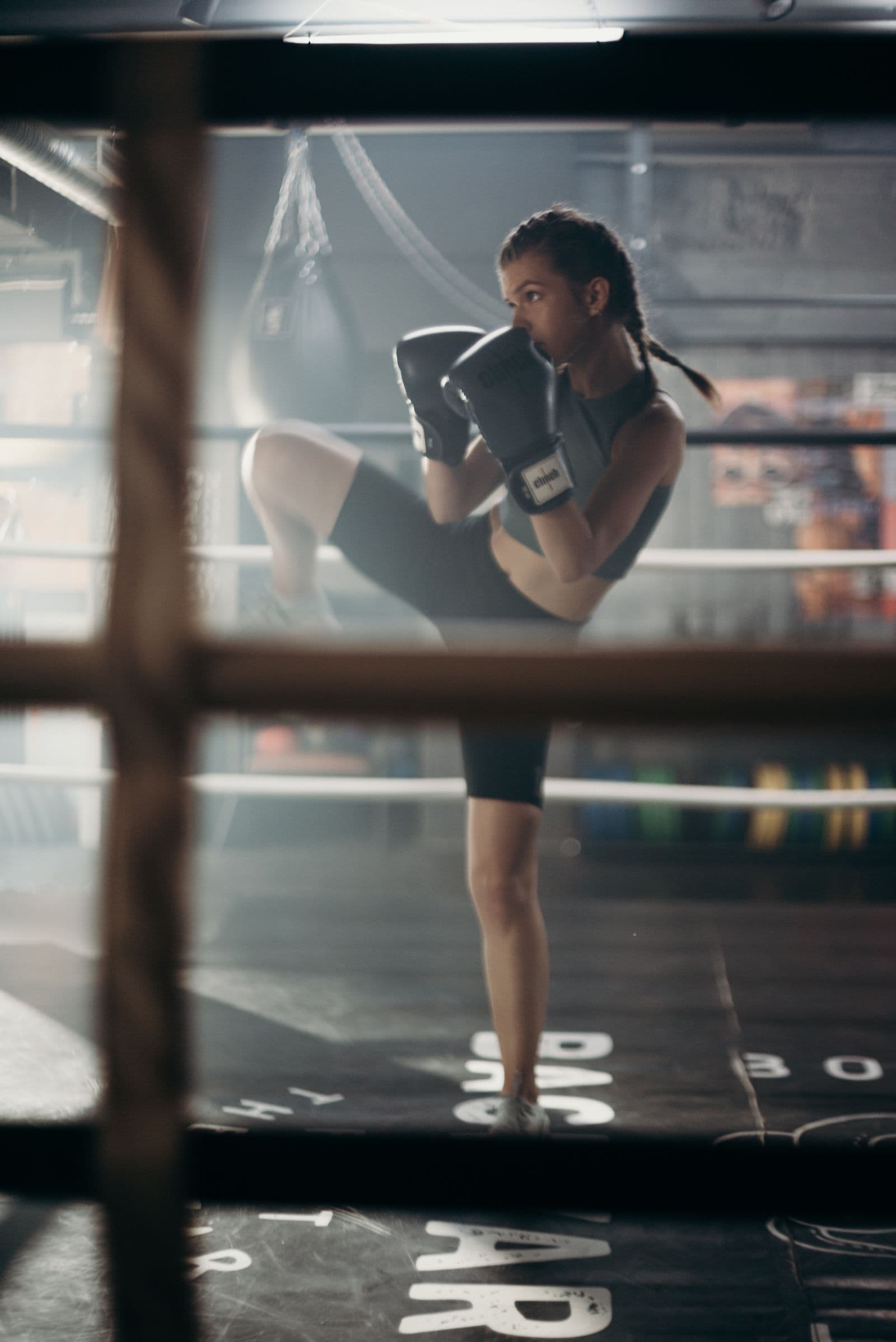 Kickboxer training in a dark gym ring, wearing black gloves and throwing a knee strike.